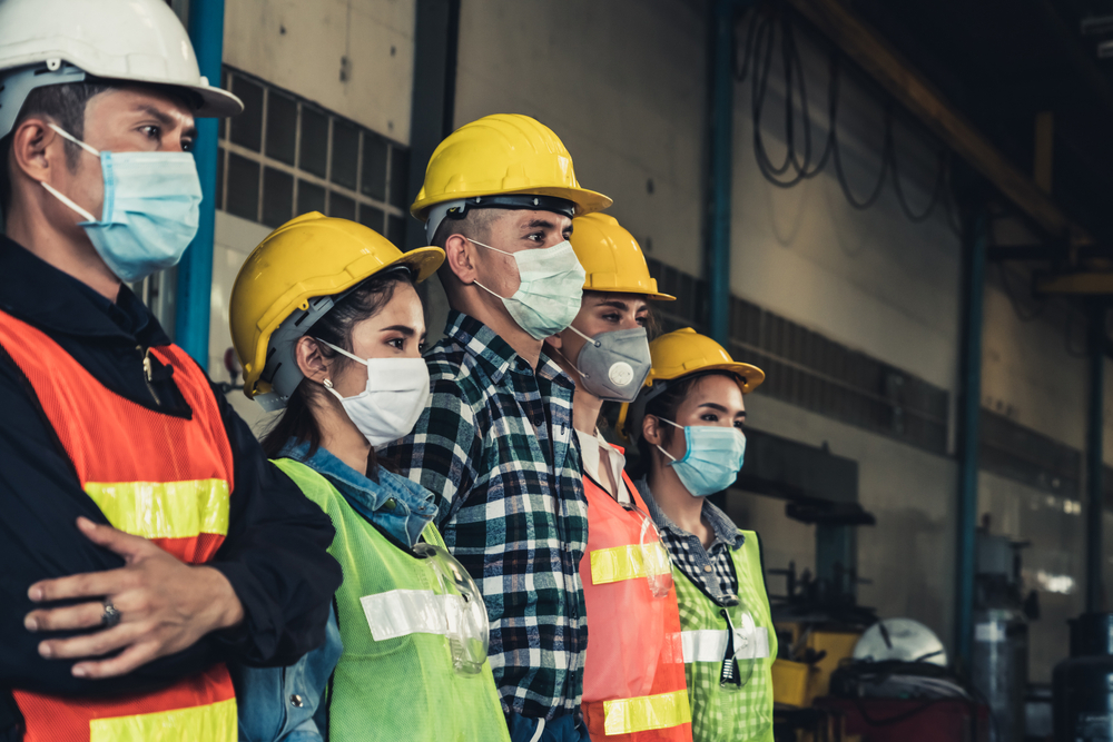 Five workers stand in line wearing PPE
