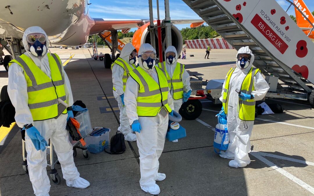 A group of cleaners wearing PPE stand in front of an aircraft