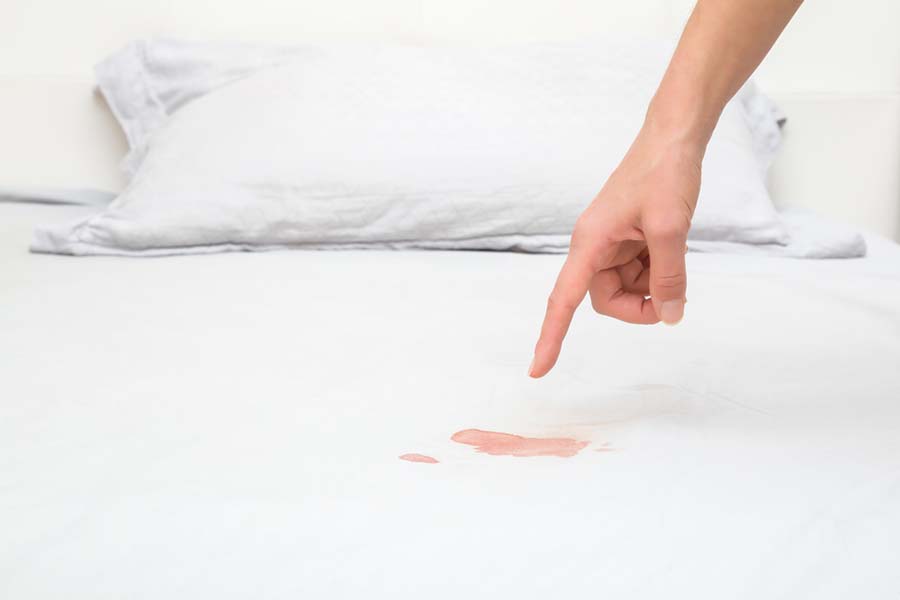 A person pointing at a blood stain on a bed mattress