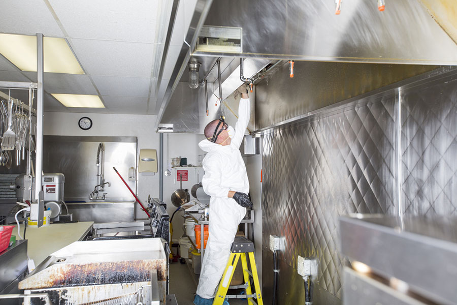 A person in PPE cleaning a commercial kitchen