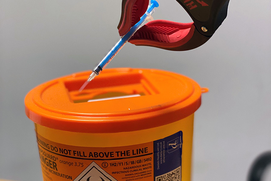 A hypodermic needle being placed into a sharps disposal bin