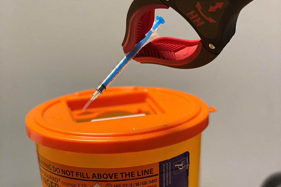 A hypodermic needle being placed safely into a sharps disposal box